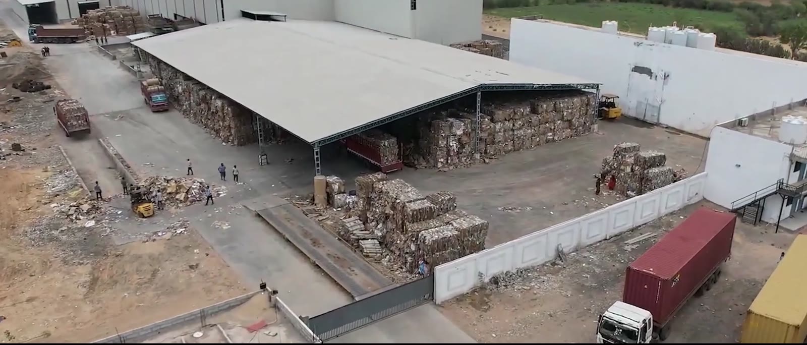 Aerial view of a Bollant recovered-paper yard with baled waste paper under a steel-framed shed and trucks at the gate