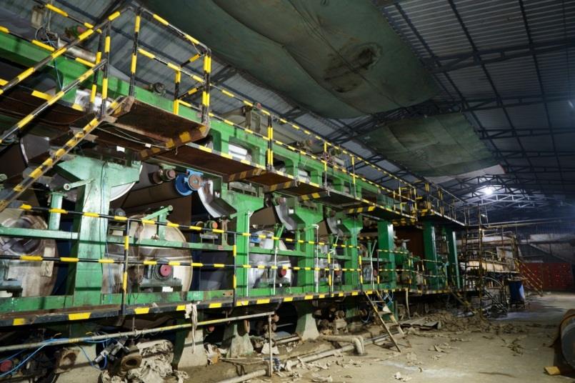 Paper machine inside a Bollant mill, with green frame, dryer cylinders and yellow safety rails